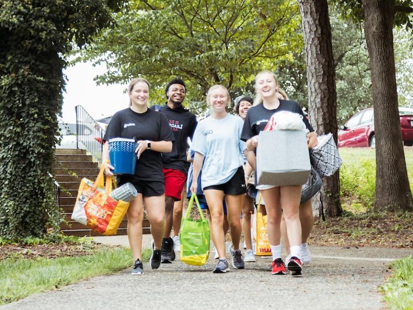 Students carry bags and boxes to a dorm during move-in.